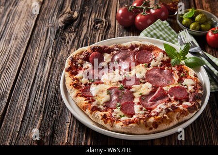 Pepperoni salami ou pizza italienne avec fromage mozzarella et basilic garnie d'herbes et servi sur une vieille table vintage rustique Banque D'Images