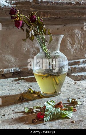 Nature morte avec roses fanées en vase en verre sur table en pierre sur une église troglodyte Banque D'Images