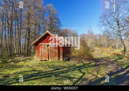 Hangar en bois rouge par une route forestière Banque D'Images