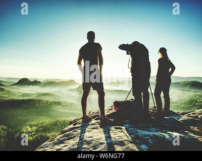 Randonneur avec deux photographes sur regarder le lever du soleil au sommet de l'horizon montagneux. Trois amis à bord de roche et de regarder les montagnes. Le voyage ou le tourisme actif FRV Banque D'Images
