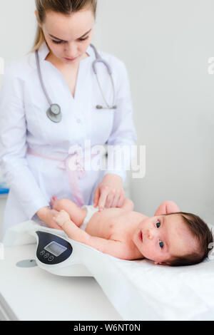 Cute little baby lying on balances, examen médical dans un centre, l'espace de copie. Jeune femme blonde médecin pédiatre examine baby girl Banque D'Images