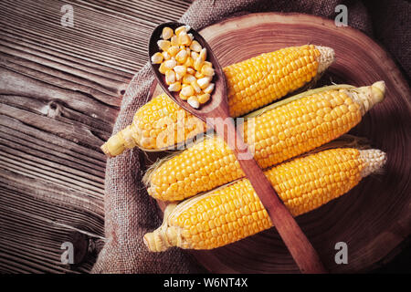 Bio sucré frais corns sur tranche d'arbre sur le sac. Les grains de maïs en épis sur la cuillère en bois. Concept de saine alimentation. Banque D'Images