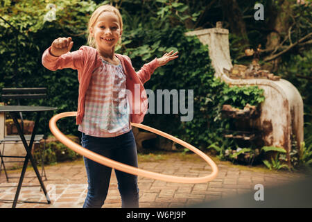 Smiling kid jouant avec un cerceau dans sa cour arrière. Girl s'amusant de tourner un anneau de tapage autour de sa taille. Banque D'Images