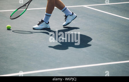Cropped shot de sportif sur un court de tennis. Joueur de tennis sur surface dure de flexion avec raquette pour aller chercher la balle. Banque D'Images