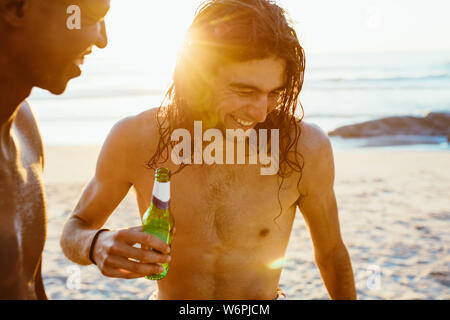 Smiling young man having beer avec ami à la plage. Deux jeunes hommes avec un café au bord de la mer. Banque D'Images