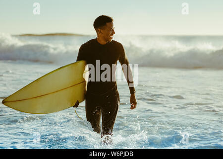Smiling Young man with surfboard sur la plage. Les hommes africains qui sortent de l'Océan surf après l'eau. Banque D'Images