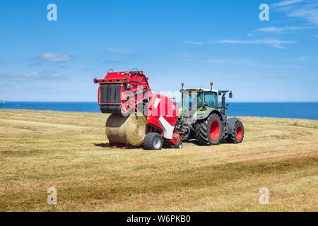 Les machines agricoles modernes - un agriculteur de tracteur en balles de foin circulaire avec un Lely Welger RP 445 une avancée variable à balles rondes. Banque D'Images