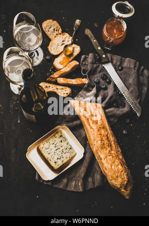 Vin et snack-set. Télévision à jeter des tranches de pain, fromage, confiture d'abricot, de petits fruits et vin blanc sur fond noir rustique, vue du dessus Banque D'Images