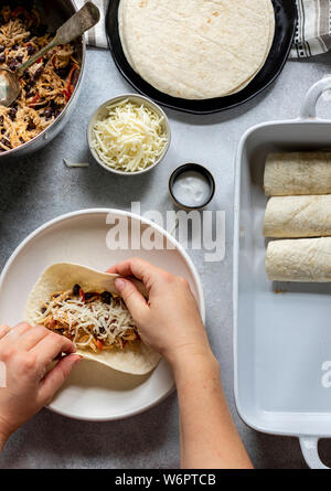 Les enchiladas en devenir. Les tortillas sur la plaque remplie de poulet au fromage et haricots noirs Banque D'Images