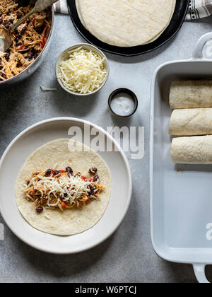 Les enchiladas en devenir. Les tortillas sur la plaque remplie de poulet au fromage et haricots noirs Banque D'Images