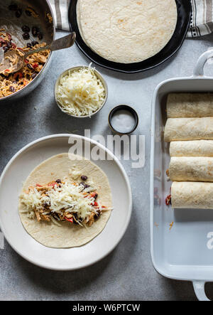 Les enchiladas en devenir. Les tortillas sur la plaque remplie de poulet au fromage et haricots noirs Banque D'Images