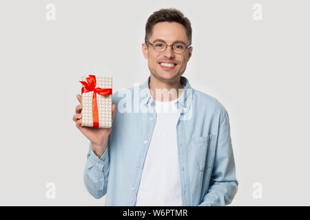 Heureux jeune homme poser sur fond gris studio holding gift box Banque D'Images