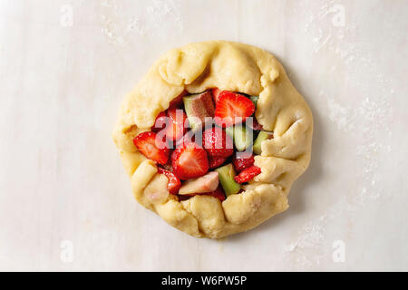 Processus d'été cuisson biscuit berry pie. Pâte sablée laminées, coupe de fraise et rhubarbe sur fond de marbre blanc. Mise à plat, de l'espace Banque D'Images