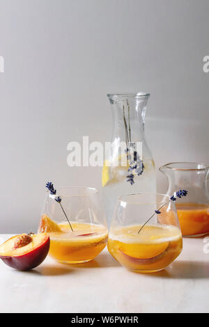 Peach Bellini cocktail froid limonade ou avec des fleurs de lavande servi dans deux verres avec cruche de jus de citron et pesh le soda sur ta en marbre blanc Banque D'Images