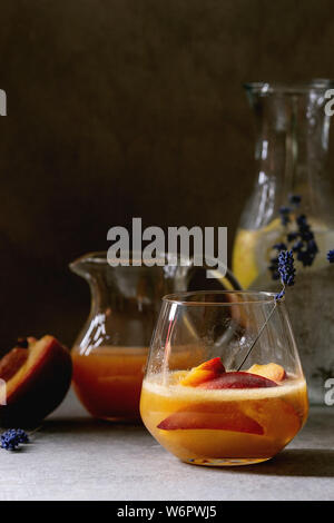 Peach Bellini cocktail froid limonade ou avec des fleurs de lavande servi dans deux verres avec cruche de jus de citron et pesh le soda sur ta texture sombre Banque D'Images