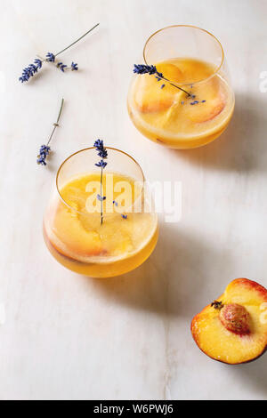 Peach Bellini cocktail froid limonade ou avec des fleurs de lavande servi dans deux verres sur la table de marbre blanc. Boisson d'été à la maison. Banque D'Images