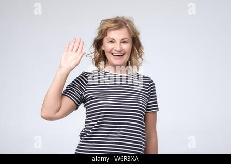 Caucasian woman smiling mature positif et amical en agitant la main at camera Banque D'Images