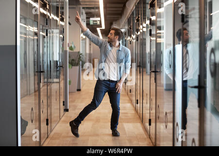 Funny heureux jeune homme d'affaires gagnant danse seul dans office hallway Banque D'Images