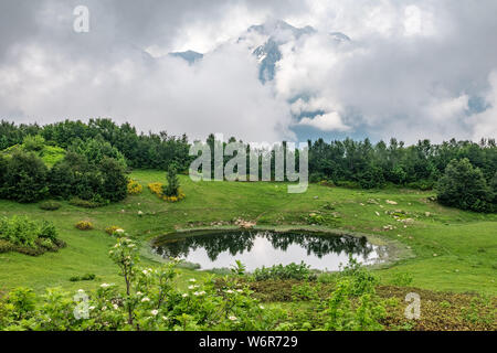 Vue d'une clairière de montagne avec un lac miroir transparent et de hautes montagnes avec des sommets enneigés au loin. Caucase, Russie Banque D'Images