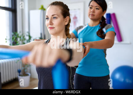 Femme chinoise professionnel physiothérapie donnant un traitement par l'utilisation de bandes de résistance élastique pour une jolie blonde client dans un bureau médical lumineux Banque D'Images