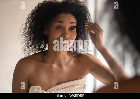 Close up mixed race woman looking in mirror le mascara Banque D'Images