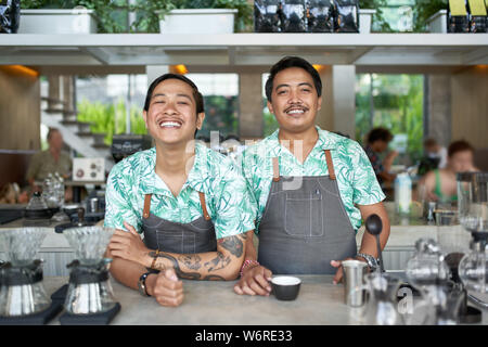 Portrait de style balinais souriant deux baristas millénaire des vêtements portant des tabliers et de hipster café servant café équitable Banque D'Images