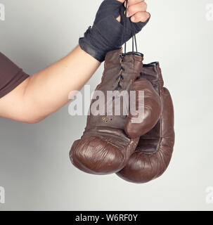 Le bras de l'homme enveloppé dans un bandage élastique noir sports détient old vintage paire gants de boxe en cuir, fond gris Banque D'Images