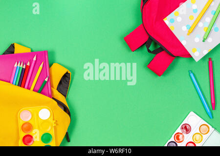 Concept Retour à l'école. Sacs à dos jaune et rose avec des fournitures scolaires, des livres et cahiers sur fond vert clair. Vue d'en haut Banque D'Images