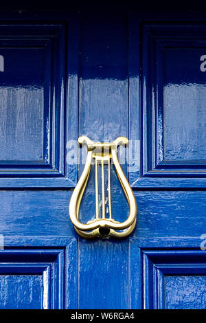 Heurtoir de porte d'or sous la forme d'une harpe irlandaise sur un porte en bois bleu foncé Banque D'Images