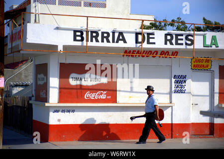 Homme portant sa guitare et une bouteille de coke framework Struts le long d'une rue à un concert passé une publicité Coca Cola à Cabo San Lucas, MX Banque D'Images