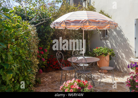 Terrasse fleurie avec mobilier de jardin en fer forgé et parasol Banque D'Images