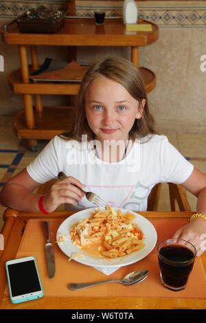 L'enfant moderne au dîner de macaroni avec sauce au restaurant. Petite fille moderne plat manger dans restaurant touristique. Petite fille profitant de l'été va Banque D'Images