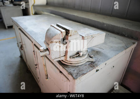Profondeur de champ libre avec un rusty et sale heavy iron vice sur un établi à l'intérieur d'un atelier avec des personnes autour de pas Banque D'Images