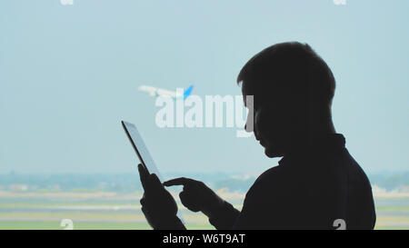 Silhouette de jeunes hommes à l'aide de tablet pc sur l'arrière-plan d'un avion au décollage. Banque D'Images