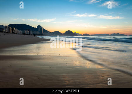 Tôt le matin, la plage de Copacabana à Rio de Janeiro avec le Mont Sugarloaf en arrière-plan juste avant le lever du soleil avec des couleurs orange et bleu Banque D'Images