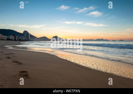 Tôt le matin, la plage de Copacabana à Rio de Janeiro avec le Mont Sugarloaf en arrière-plan juste avant le lever du soleil avec des couleurs orange et bleu Banque D'Images