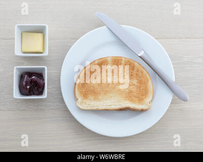 Une assiette petit-déjeuner toast beurre confiture couteaux jelly sur table en bois Banque D'Images