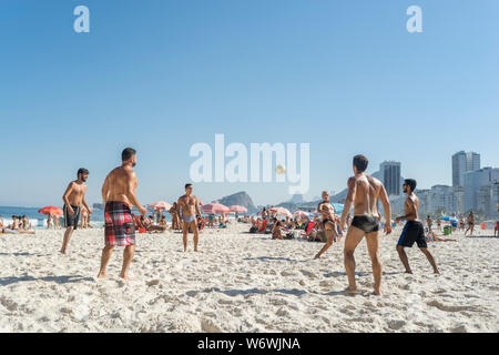 Groupe de jeunes jouant pied volley sur la plage de Copacabana sur une journée ensoleillée avec ciel bleu avec décor quartier typique Banque D'Images