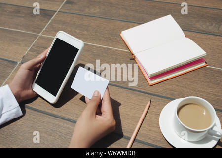 Close up woman holding credit card et écran blanc mobile phone sitting at coffee shop Banque D'Images