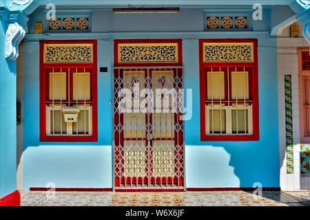 Entrée de maison traditionnelle boutique Peranakan rouge et crème avec porte et fenêtres sur mur bleu avec des ombres et de la lumière du soleil dans la ville historique de Geylang Singapore Banque D'Images