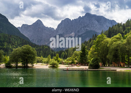 La Slovénie, Triglav - Août 28, 2017 : Les gens de soleil sur ponton en bois au lac Jasna, avec des pics de montagne des Alpes Juliennes en arrière-plan. Banque D'Images