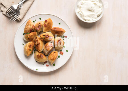 Boulettes frites farcies de viande et de pommes de terre (pierogi) saupoudré de bacon et le persil et la crème fraîche sur la table en bois blanc, copie de l'espace. Banque D'Images