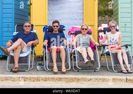 Bournemouth, Dorset Royaume-Uni. 3 août 2019. Météo au Royaume-Uni : couvert et nuageux, mais chaud et brumeux. Les amateurs de plage se rendre sur les plages de Bournemouth pour profiter du temps chaud. Quatre personnes se détendant dans des chaises longues sur la promenade en dehors des cabanes de plage. Crédit: Carolyn Jenkins/Alay Live News Banque D'Images