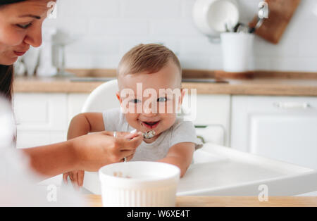 Charmant petit baby boy eating première nourriture de porridge spoon à la cuisine. Maman rss enfant Banque D'Images