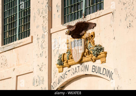 L'écaillage de la peinture et un emblème pâle ornent la façade de l'ancien bâtiment de l'Administration pénitentiaire d'Alcatraz pour sur le "Rocher" dans la baie de San Francisco Banque D'Images