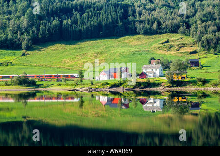 Un train qui passait l'été norvégien traditionnel ferme le long du lac Vangsvatnet reflète dans l'eau près du comté de Hordaland en Norvège Voss Banque D'Images