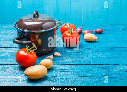 Photo de pot de fer pour la soupe, tomates, pommes de terre, oignons sur fond en bois bleu. Banque D'Images