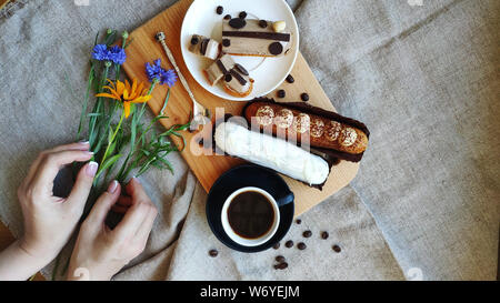 Vue de dessus sur les mains avec des fleurs d'rutbeckia bleuet et près de tasse de café noir et des éclairs servi, le concept d'un petit déjeuner agréable Banque D'Images