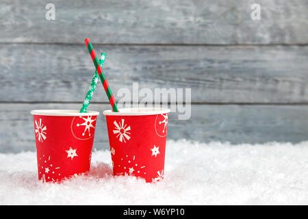 Deux tasses rouge papier de Noël avec boisson dans la neige sur fond de bois Banque D'Images