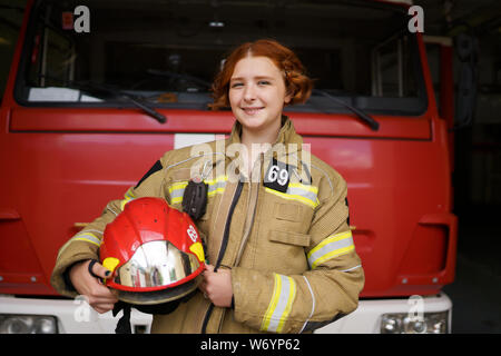 Photo de femme pompier avec casque dans les mains contre fond de camion d'incendie Banque D'Images